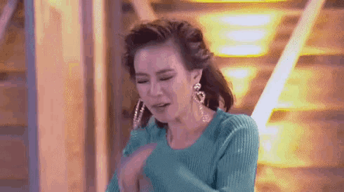a woman wearing a blue sweater and earrings is standing in front of a staircase .