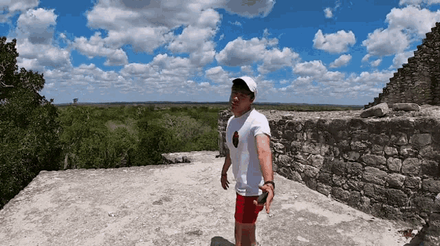 a man in a white shirt and red shorts stands on top of a stone wall