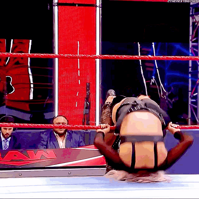 a man in a suit sits in the stands watching a woman in a wrestling ring with the word raw in the corner