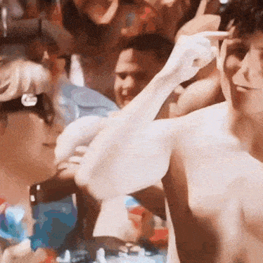 a man without a shirt is standing in front of a crowd of people and pointing at something .