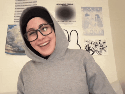 a woman wearing glasses and a hooded sweatshirt with a poster on the wall that says edward rudoe on it