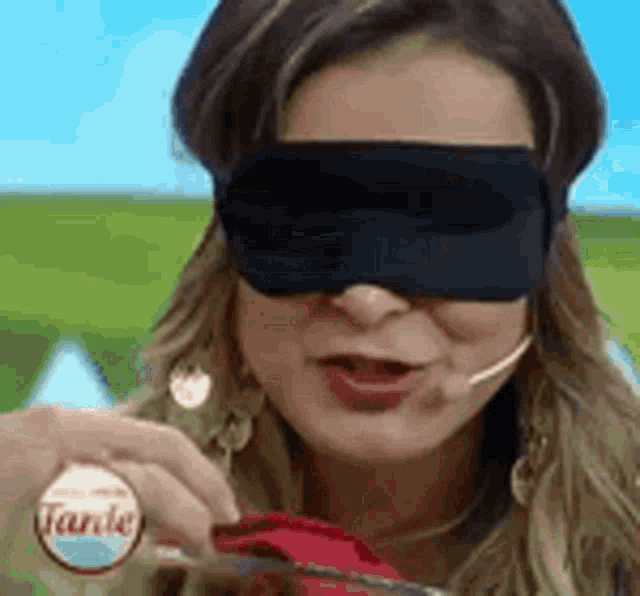 a woman wearing a blindfold and a microphone is holding a knife and fork .
