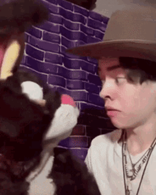 a man wearing a hat and a necklace is looking at a stuffed animal