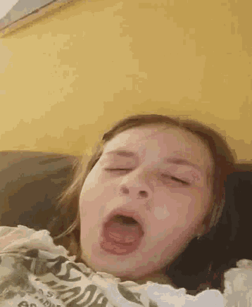 a little girl is yawning with her mouth open while laying on a couch .