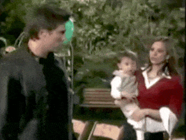 a man and a woman holding a baby in front of a bench