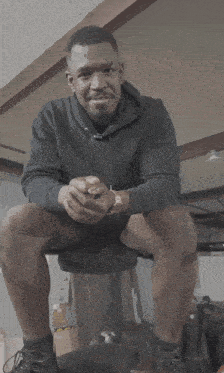 a man in a black hoodie is sitting on a chair with his legs crossed