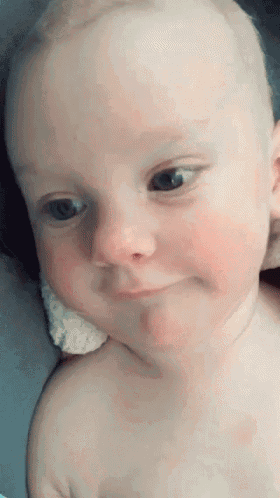 a baby without a shirt is looking at the camera and smiling