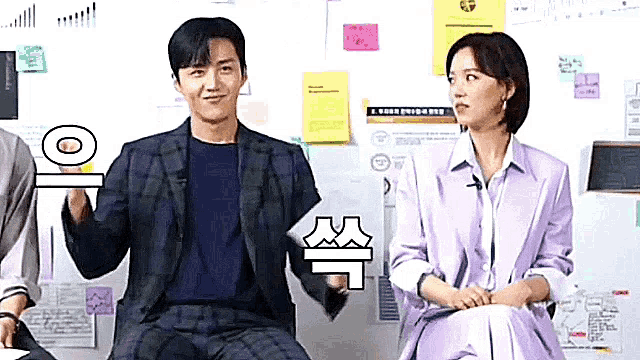 a man in a suit and a woman in a purple dress are sitting next to each other in front of a wall .