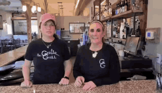 two women wearing shirts that say the grotto grill stand behind a counter