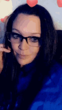 a woman wearing glasses and a blue sweater is smiling