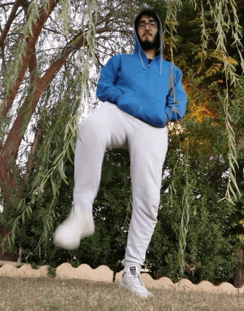 a man wearing a blue hoodie and white sweatpants is standing in the grass