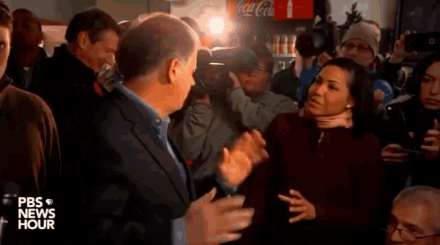 a man in a suit talks to a woman in front of a coca cola cooler