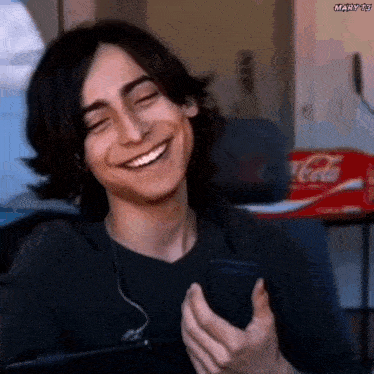 a young man with long hair is smiling while holding a cell phone .