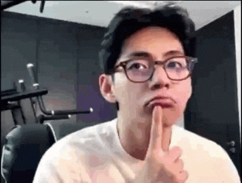 a man wearing glasses is making a funny face while holding his finger to his lips .