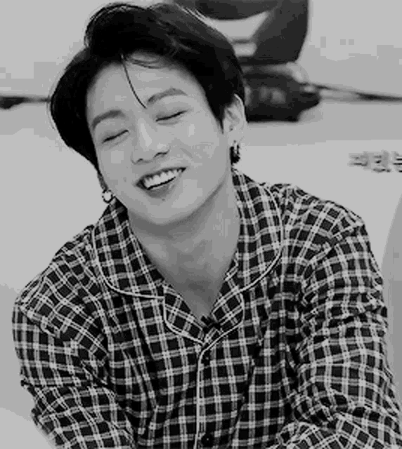 a black and white photo of a young man wearing a plaid shirt and earrings .