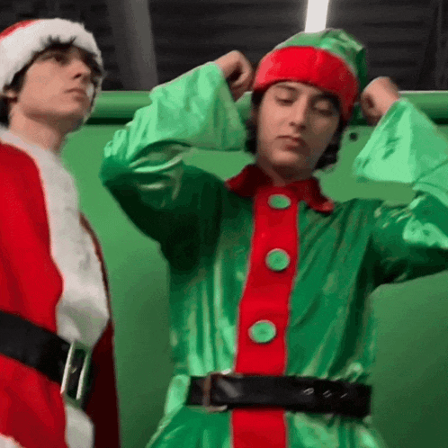 a man dressed as an elf is flexing his muscles next to another man dressed as santa