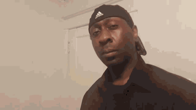 a man wearing a black adidas hat stands in front of a white wall