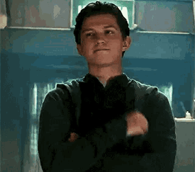a young man in a black sweater is standing with his arms crossed in a room .