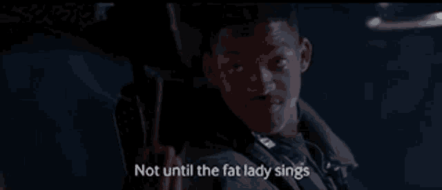 a man is holding a gun in a dark room and saying not until the fat lady sings .