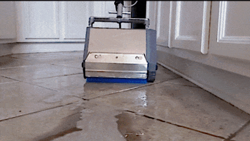a machine is cleaning a tiled floor with a blue brush