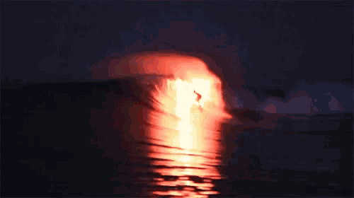 a person riding a wave in the ocean at night with a red light behind them