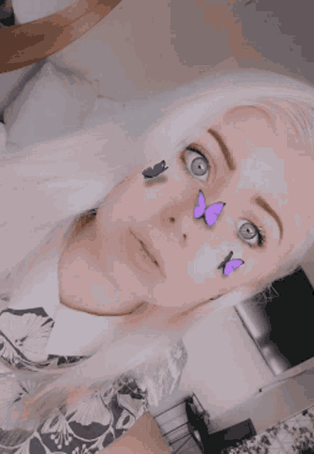 a woman with purple butterflies on her face looks at the camera