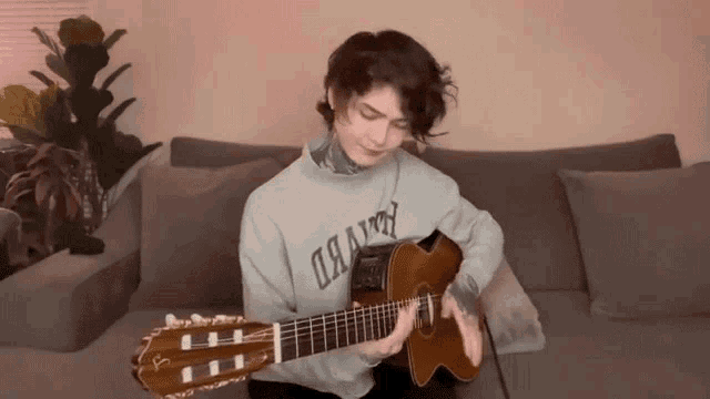 a young man is playing a guitar while wearing a grey sweater that says " i have "