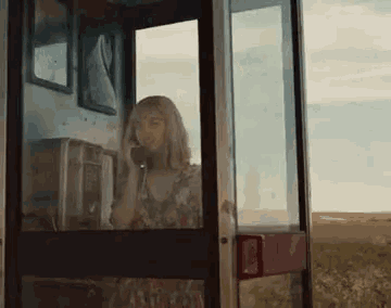 a woman is sitting in a pay phone booth talking on a cell phone .