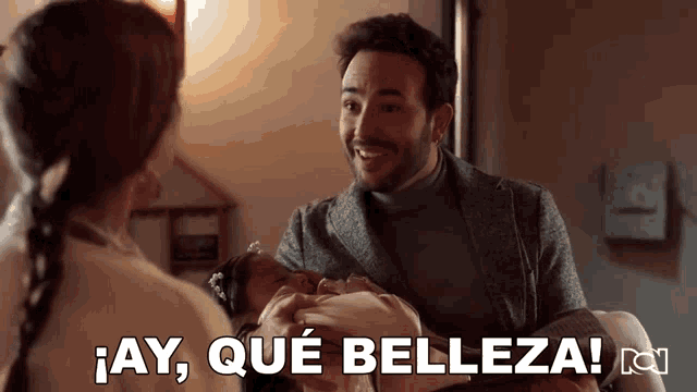 a man holding a baby with the words " ay que belleza " written below him