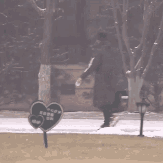 a person wearing a black jacket with a white lettering on the sleeve is running in the snow near a tree