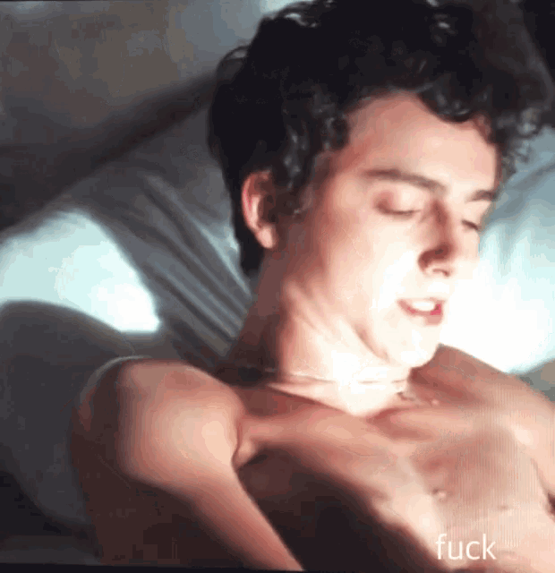 a shirtless man is laying on a bed with his eyes closed and the word fuck written below him