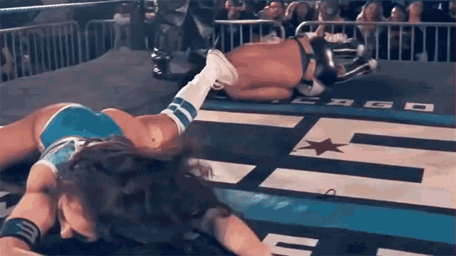 two women are wrestling in a ring and one of them is laying on the ground .