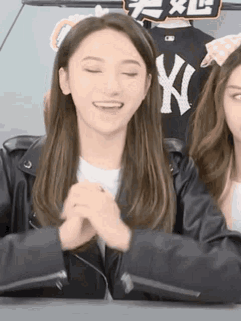 a woman wearing a black ny yankees jacket is smiling while sitting next to another woman .