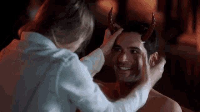 a woman is putting horns on a man 's head in a dark room .