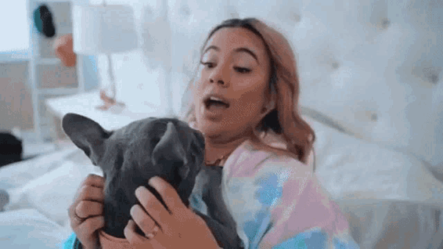 a woman is laying on a bed holding a dog and kissing it .