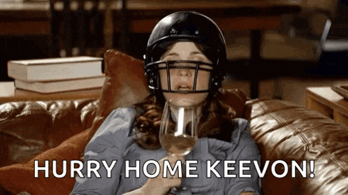 a woman wearing a football helmet is sitting on a couch drinking wine .