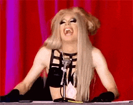 a drag queen is sitting at a table with a microphone and laughing .