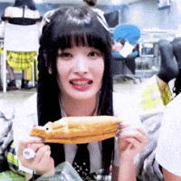 a woman with long black hair is holding a sandwich in her hands and smiling .