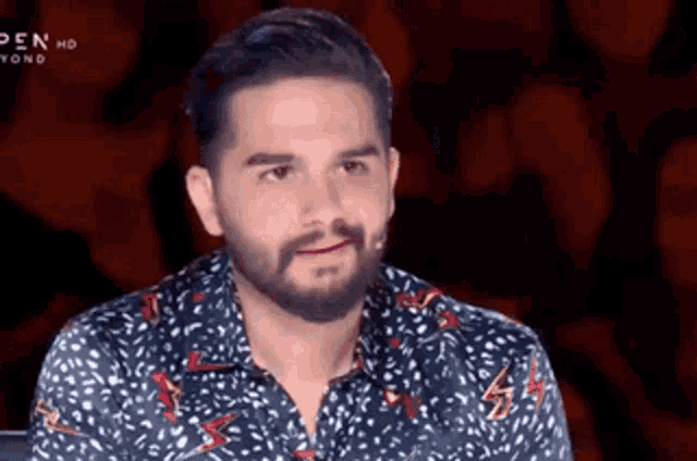 a man with a beard is sitting in front of a crowd wearing a polka dot shirt .