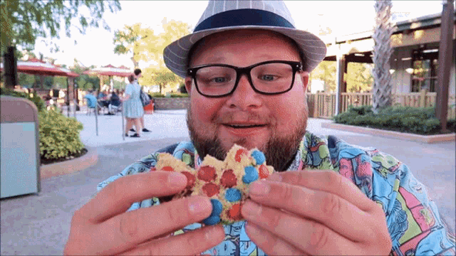 a man wearing glasses and a hat holds a cookie in his hands