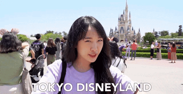 a woman in a purple shirt is standing in front of a castle and the words tokyo disneyland