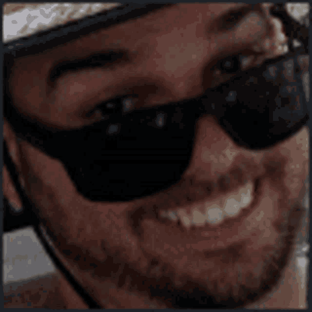 a man wearing sunglasses and a hat is smiling for the camera .