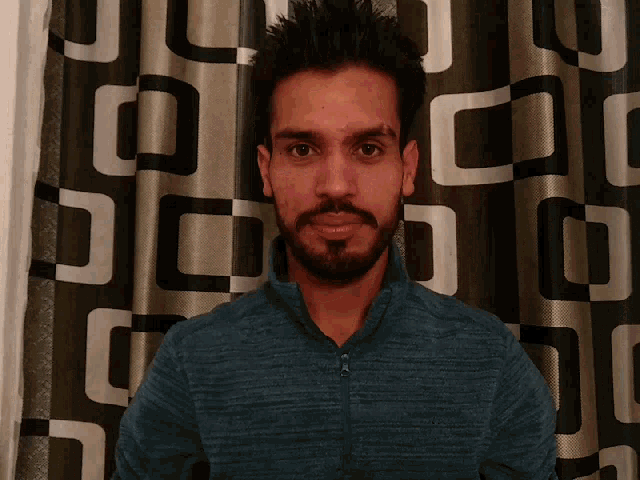 a man with a beard is standing in front of a curtain