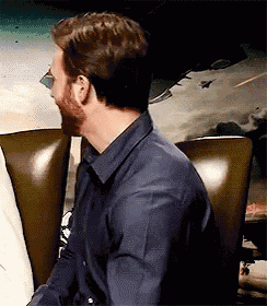 a man with a beard is sitting in a chair looking at something .
