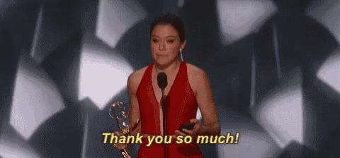 a woman in a red dress is holding a microphone and saying `` thank you so much '' while holding a trophy .