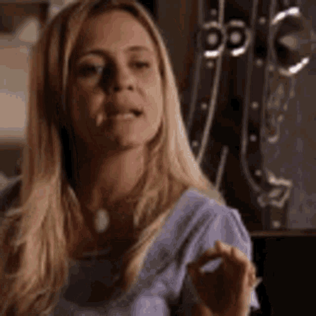 a woman with blonde hair is wearing a purple shirt and making an okay sign .