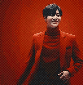 a man in a red suit and black turtleneck is dancing in front of a red wall .