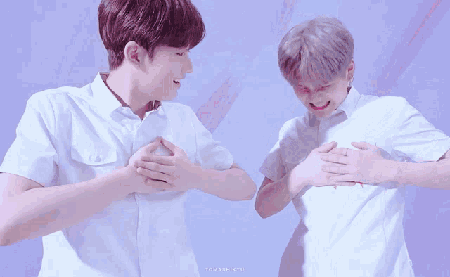 two young men in white shirts are holding their chests together and one of them is smiling
