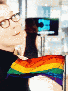 a man wearing glasses holds a rainbow flag in his hand