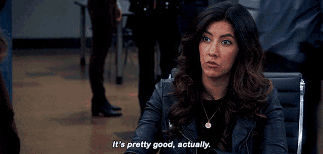 a woman in a leather jacket is sitting in a chair and saying it 's pretty good actually